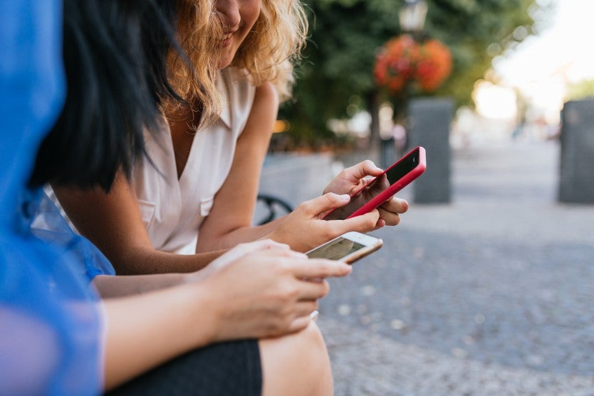 Close up of two girls holding their smartphone outdoor. Technology and friendship concept
